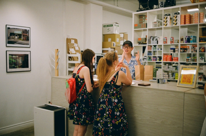 A friendly retail employee actively engages two customers at a modern shop counter, surrounded by organized product shelves, reflecting strong customer service and effective sales interactions.