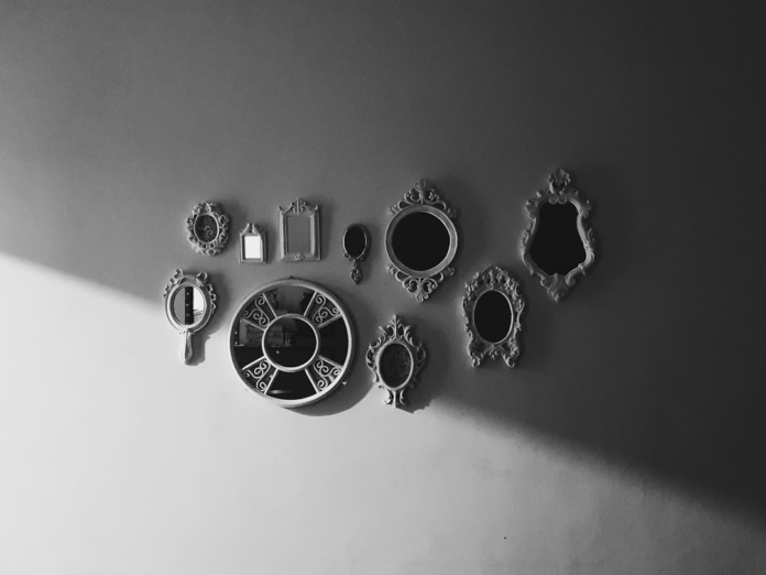A black and white collection of antique-style mirrors in varied shapes on a wall, with a strong diagonal shadow, symbolizing multiple perspectives for marketing and sales alignment and business growth.