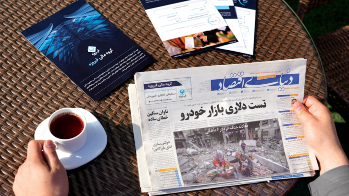 Hands holding a newspaper, a cup of tea, and various financial publications on a sunlit wicker table, depicting a focused moment of content discovery.