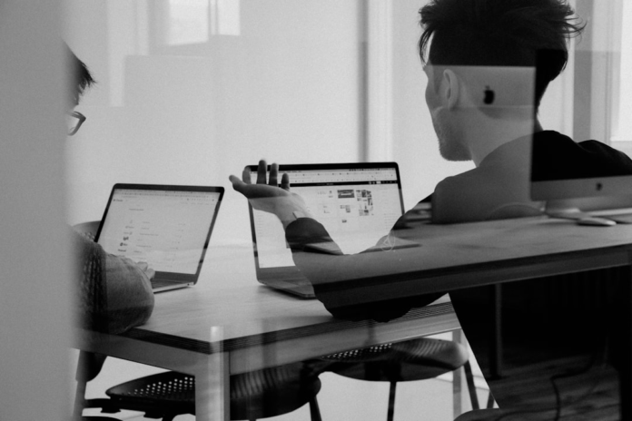 Two people collaboratively engaging with laptops in a modern black-and-white office, suggesting interactive discussion for online learning strategies.