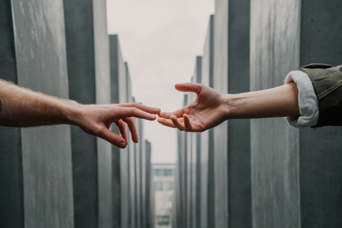 Hands reaching out to connect, illustrating the intentional effort required to build lasting customer relationships and trust against a backdrop of tall, structured grey pillars.