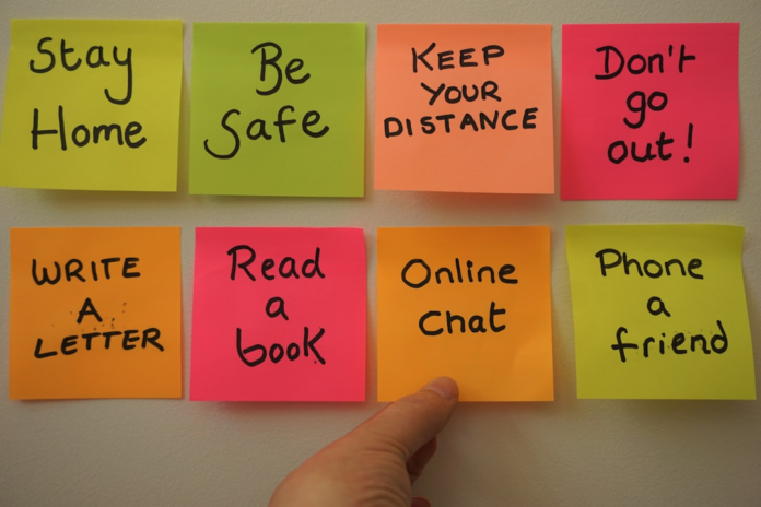 A hand adjusts one of several colorful sticky notes on a wall, displaying a mix of urgent safety warnings and engaging communication reminders, visually representing organized key messages and actionable content for effective email marketing campaigns.