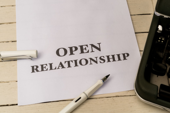 White paper prominently displaying the bold text OPEN RELATIONSHIP, with a white fountain pen and a partial view of a vintage typewriter resting on a light wooden desk, illustrating a focus on establishing clear customer relationships.