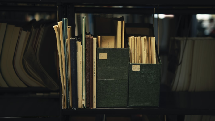 A neatly organized shelf holds various aged books and two dark green archival boxes, representing diligent data organization and the careful maintenance of records for effective list hygiene.