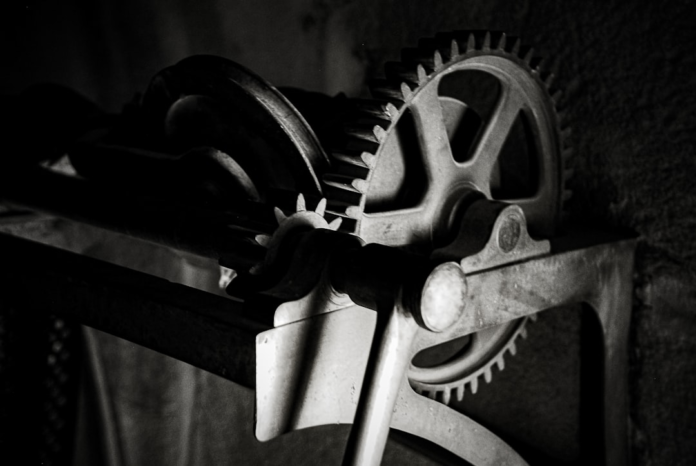 A stark black and white image features a large, spoked gear meshing with smaller industrial cogs, symbolizing the intricate internal processes of system troubleshooting and optimization.