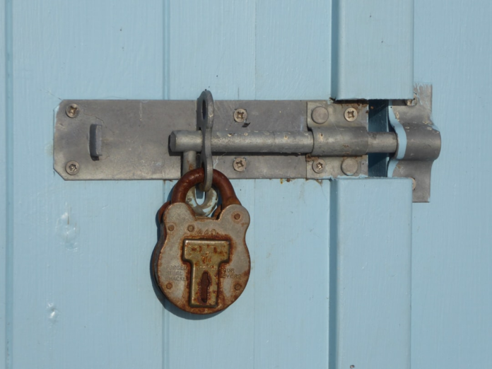 Close-up of a weathered metal bolt and rusty padlock securing a light blue wooden door, symbolizing robust data protection and GDPR compliance.