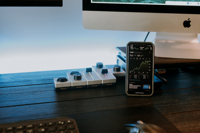 A smartphone displaying an upward-trending performance graph sits on a modern dark wood desk alongside a modular control panel, symbolizing data-driven insights and strategic growth for maximizing marketing ROI.