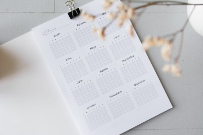 A minimalist annual calendar planner with months in Spanish, secured by a binder clip on a light gray desk, ideal for organizing blogging and newsletter content strategies.