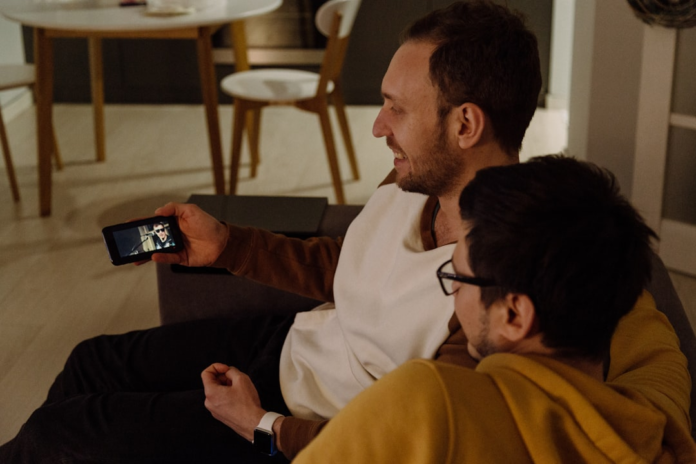 Two people relax on a sofa, focused on engaging video content displayed on a smartphone, illustrating the reach of online video marketing.