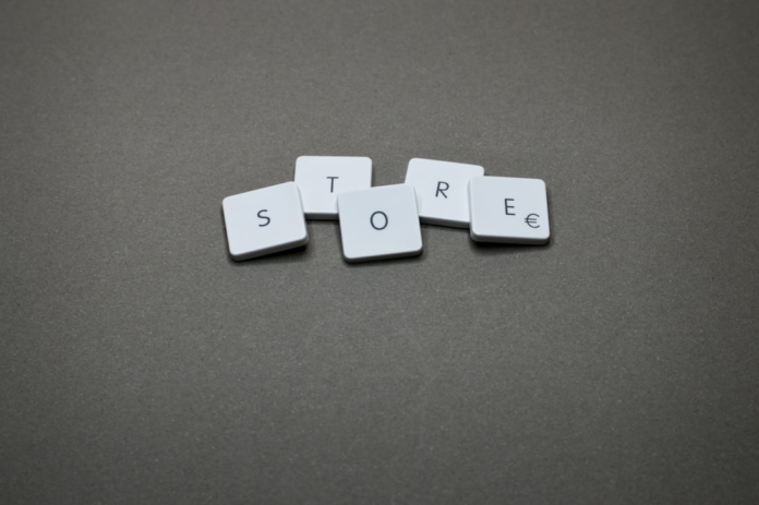 White square tiles spelling STORE with a Euro symbol on the 'E' are laid out on a dark grey surface, conveying the foundational concept of launching an e-commerce business.