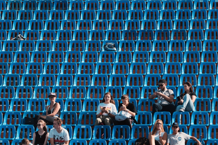 Spectators are scattered across rows of bright blue stadium seats, with many focused on their mobile phones, symbolizing a vast, digitally engaged audience for online video content.