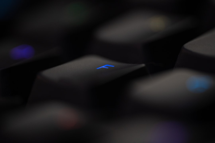 Close-up of a dark, modern backlit computer keyboard featuring a blue-illuminated 'F' key, representing the digital communication tools used for real estate email marketing.