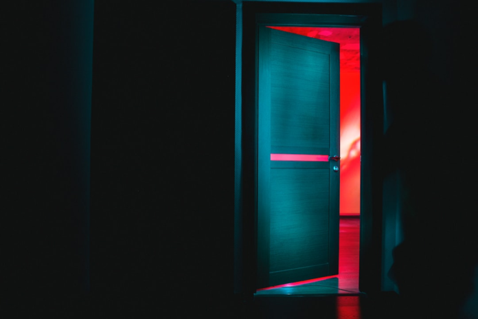 Dark hallway facing a teal door slightly ajar, revealing a vibrant red-lit room beyond, symbolizing new pathways and unlocked industry potential with Salesforce Vlocity.