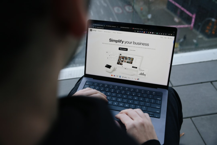 A person intently types on a laptop displaying a SumUp business dashboard with sales and payment solutions, representing the essential digital tools for successful Shopify store management against a blurred urban backdrop.