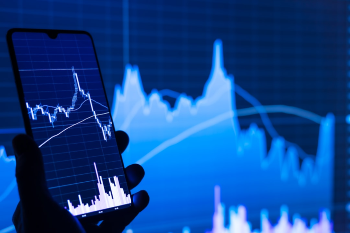A hand holds a smartphone displaying glowing blue performance data charts, with a large, blurred graph backdrop, symbolizing in-depth analysis of Sendinblue (Brevo) pricing and features.