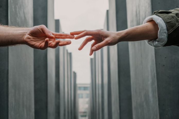 Close-up of two hands reaching out to one another, almost touching, against a backdrop of tall, grey rectangular pillars, symbolizing the essential connection in remarketing campaigns to non-openers.