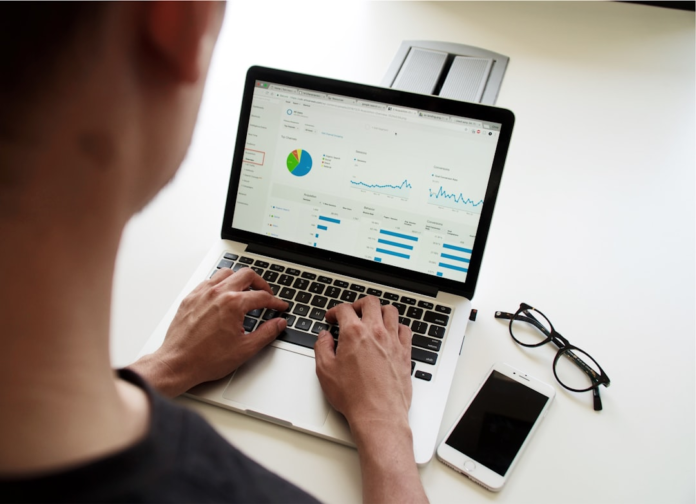 Focused person analyzing website performance data on a laptop displaying Google Analytics charts, with glasses and a smartphone on a clean white desk, illustrating effective Shopify and Google Search Console management.