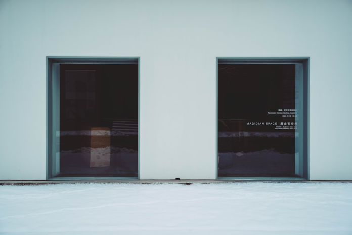 Sleek, minimalist building exterior with two dark, reflective window panels, one displaying MAGICIAN SPACE text, set against a pristine snow-covered foreground, evoking a sense of refined, optimized design.