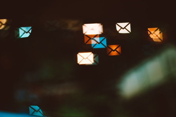 Glowing, abstract email envelope icons in orange, white, and blue bokeh float on a dark background, symbolizing digital messages and newsletter communication.