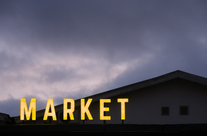 Illuminated yellow MARKET sign glows brightly against a dark, cloudy evening sky and building, signifying the essential space for commerce and sales.