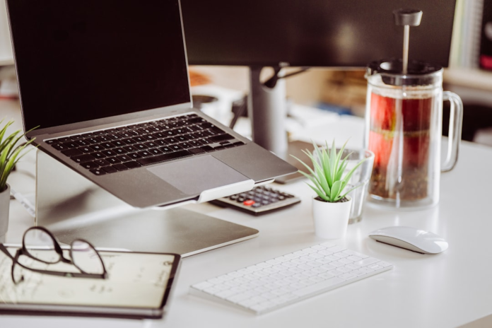Productive desk setup featuring a laptop on a stand, external keyboard, mouse, calculator, and a French press, indicative of a dedicated space for YouTube content creation and monetization strategies.